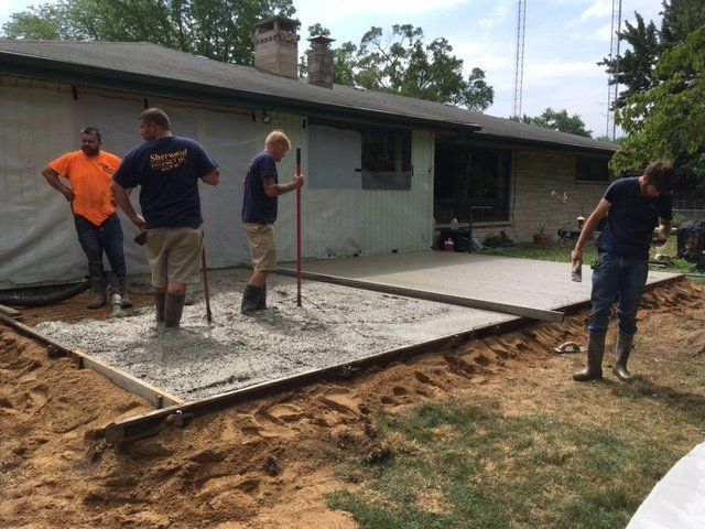 Workers pouring and leveling a concrete patio beside a house