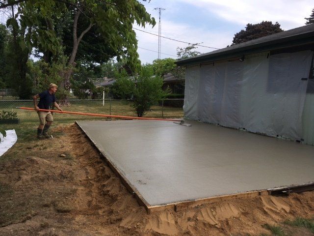 Worker smoothing wet concrete slab beside a house in a yard