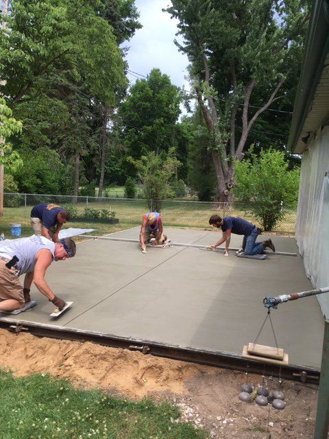 Workers smoothing a concrete slab beside a house in a leafy yard