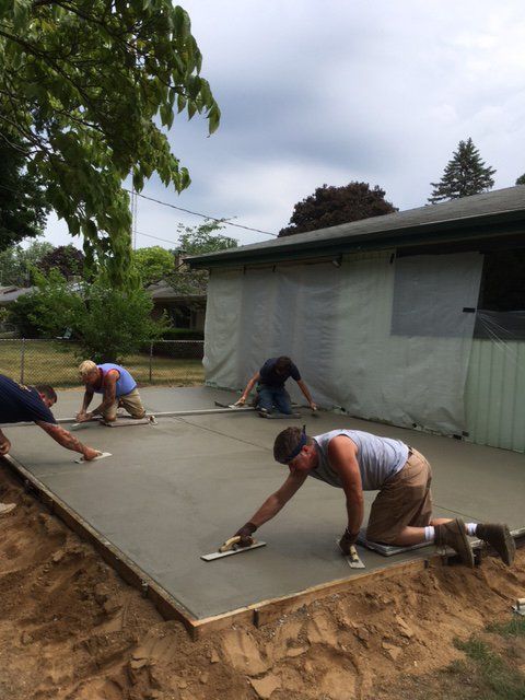 Workers smoothing concrete slab beside a house under construction