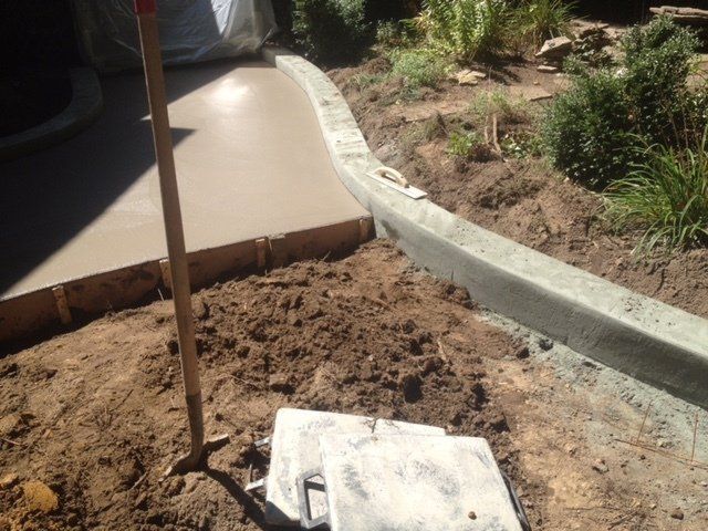 Dirt beside a concrete walkway with a shovel and a curb edge under construction