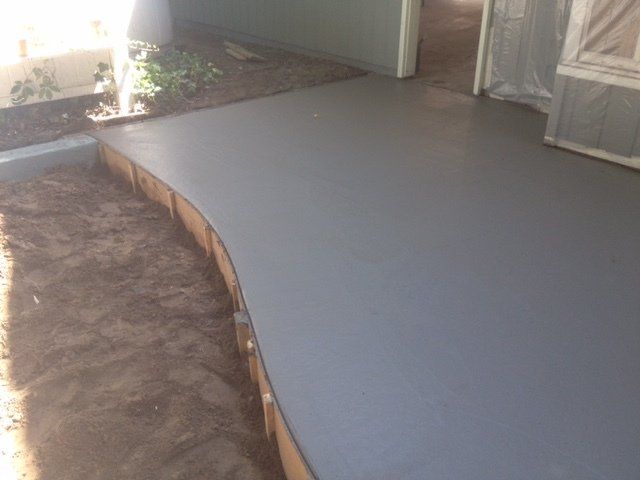Concrete patio with a curved edge beside a dirt yard and screened porch doors