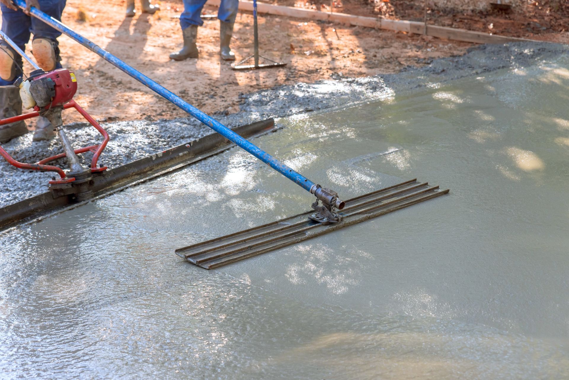 Construction workers smoothing wet concrete with a blue-handled screed on a driveway