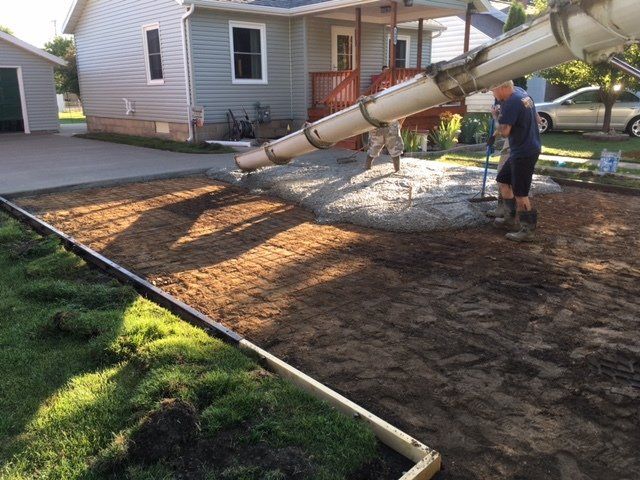 Concrete is being poured into a driveway beside a house, with workers leveling it.