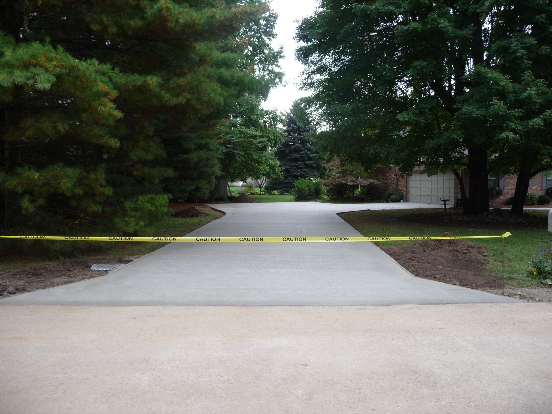 Driveway blocked by yellow caution tape between trees and houses.