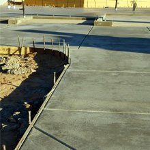 New concrete sidewalk beside a construction area with exposed dirt and rebar traces