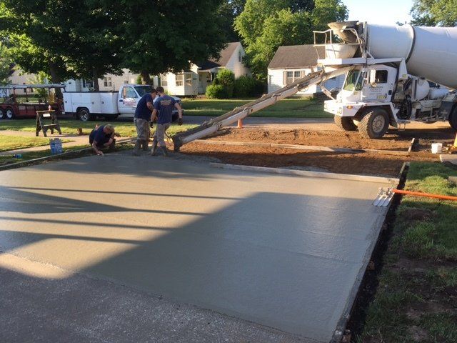 Workers pour fresh concrete into a residential driveway from a mixer truck.