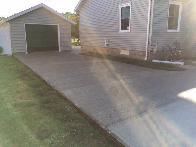 Driveway leading to an open detached garage beside a beige house on a sunny day