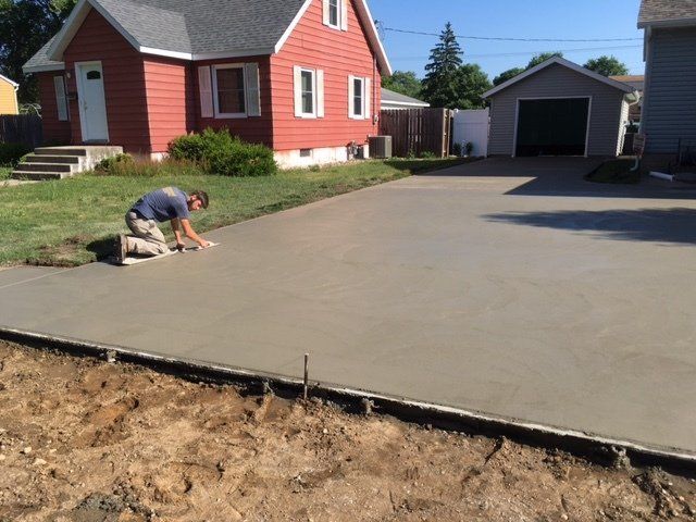 Worker smoothing fresh concrete driveway beside a red house and garage on a sunny day