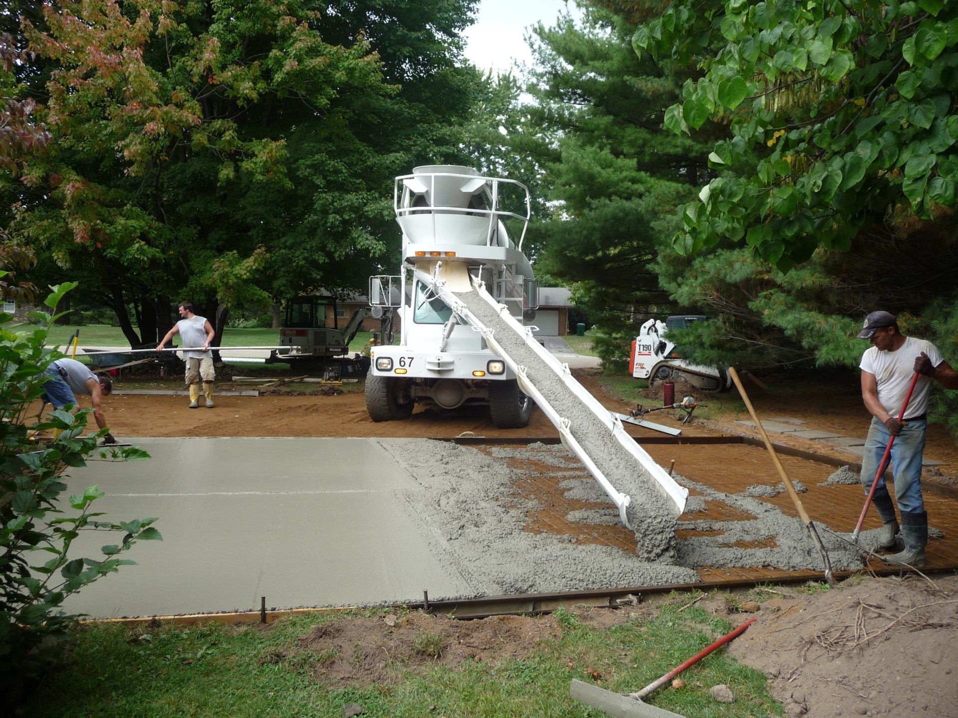 Concrete mixer truck pouring cement at a muddy roadside construction site with workers nearby