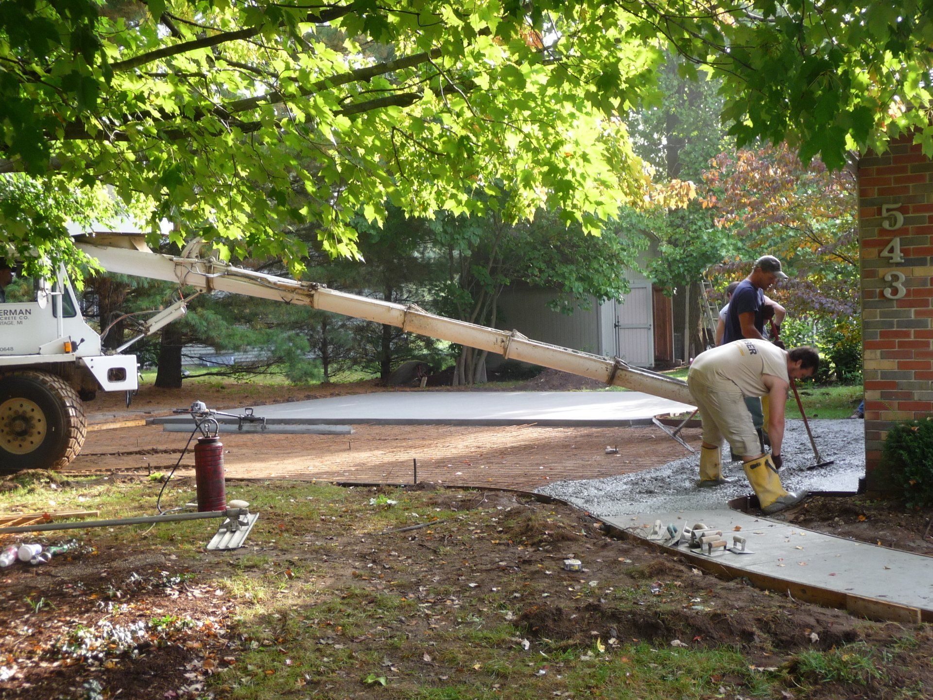 Workers removing a fallen tree branch from a residential sidewalk with a truck and bucket lift nearby