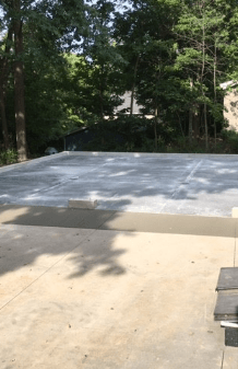 Concrete slab in a wooded yard, with trees and a house visible in the background.