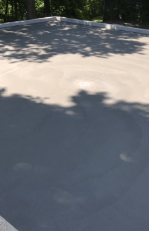 Flat light-gray roof with tree shadows in sunlight