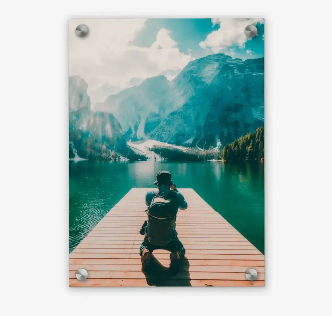 A man with a backpack is kneeling on a dock overlooking a lake in an acrylic print hanging on a wall.