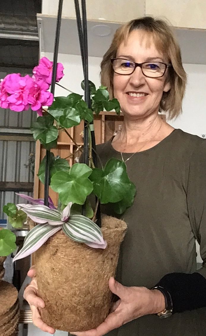 A woman is holding a potted plant with pink flowers.