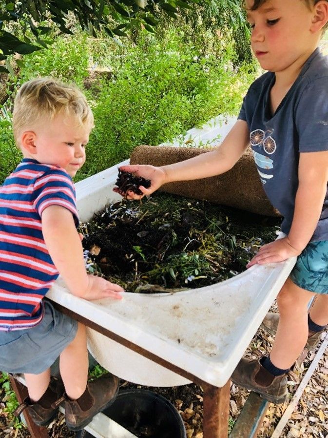 Two young boys are playing with a bowl of dirt.