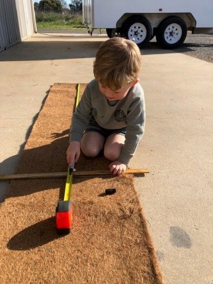 A young boy is measuring a piece of wood with a tape measure.