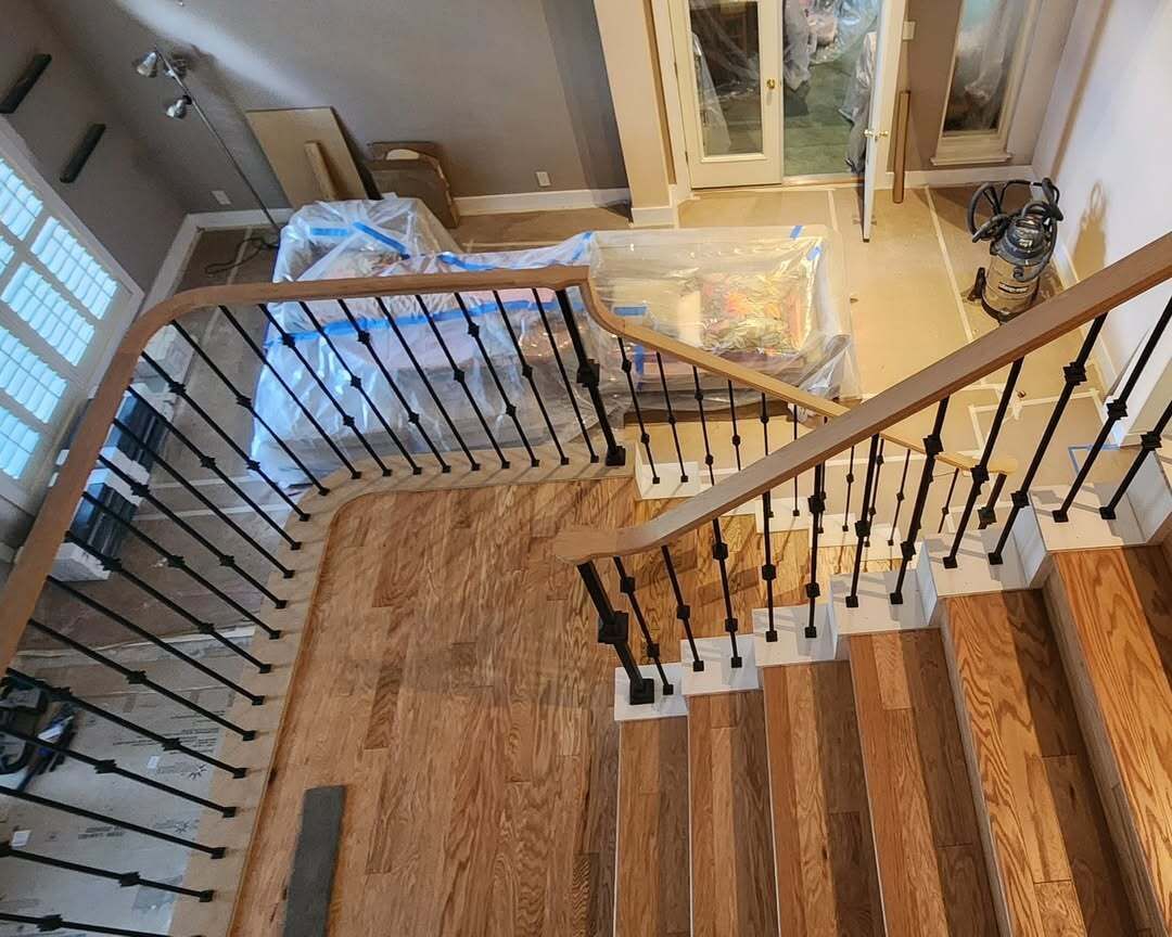 Staircase landing with wooden floors, black railing, and a view into the lower level during renovation