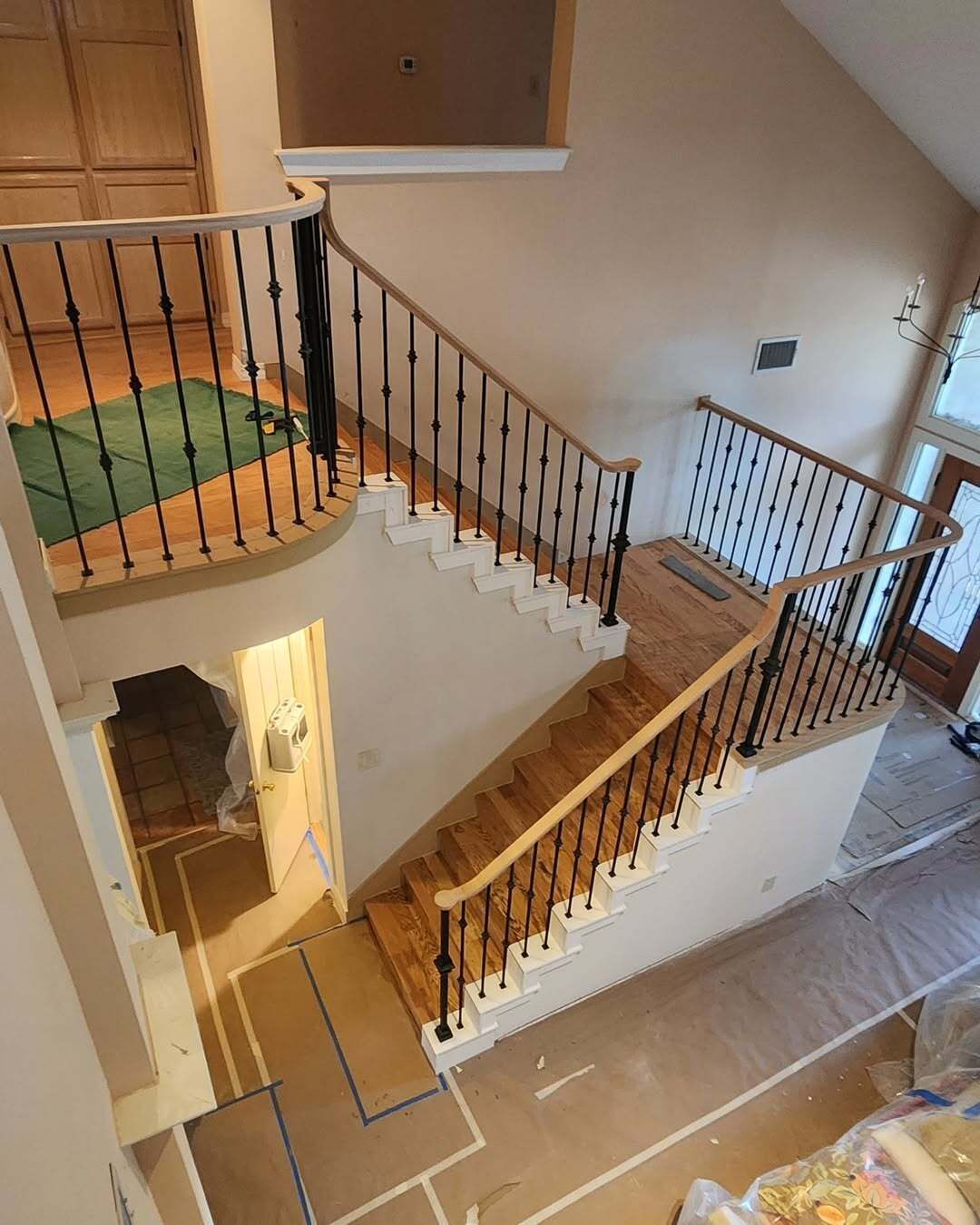 Indoor staircase with black railings, beige walls, and a small balcony landing above a tiled floor.