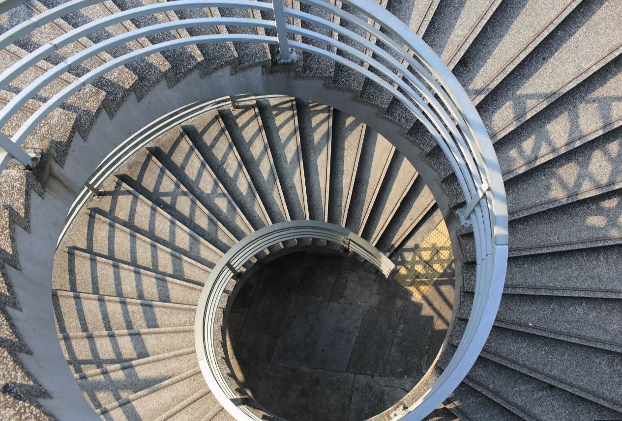 Top-down view of a spiral staircase with gray steps and blue railings around a circular opening