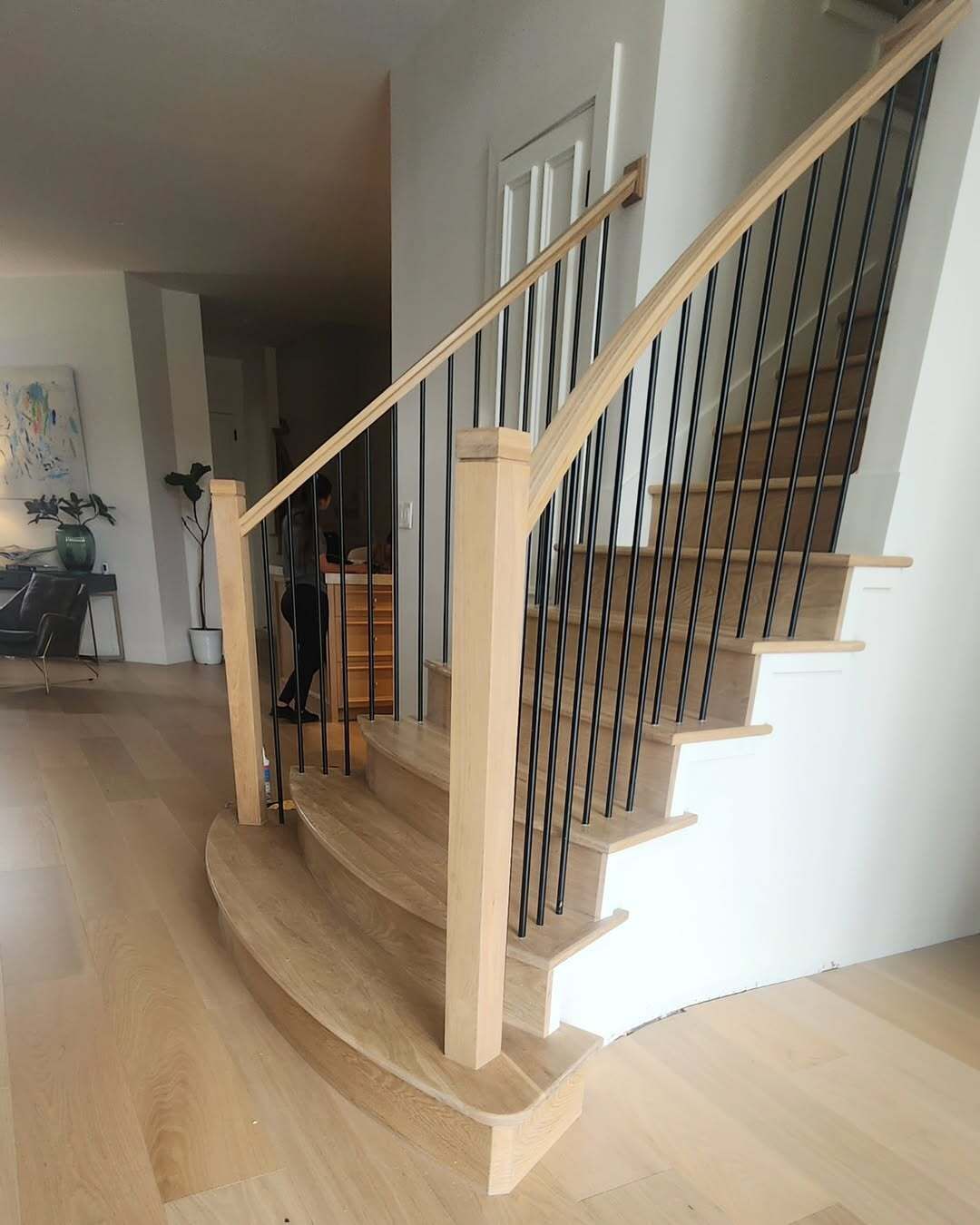 Curved wooden staircase with black railing in a bright home interior