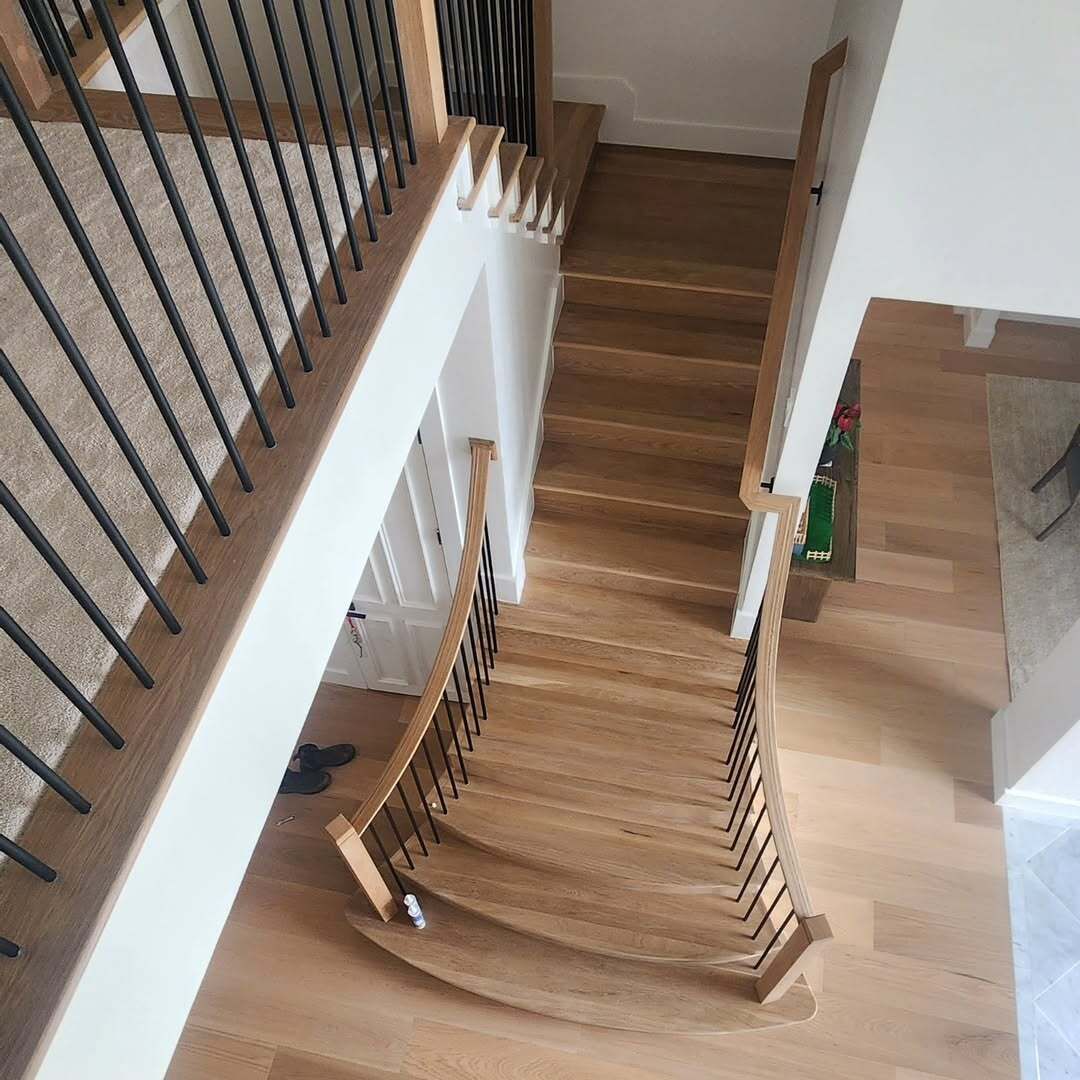 Top-down view of a wooden staircase with black railings in a bright home interior