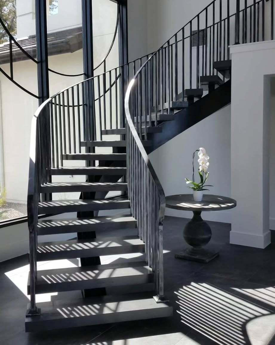 Black spiral staircase with metal railing in a bright indoor entryway beside a small round table.