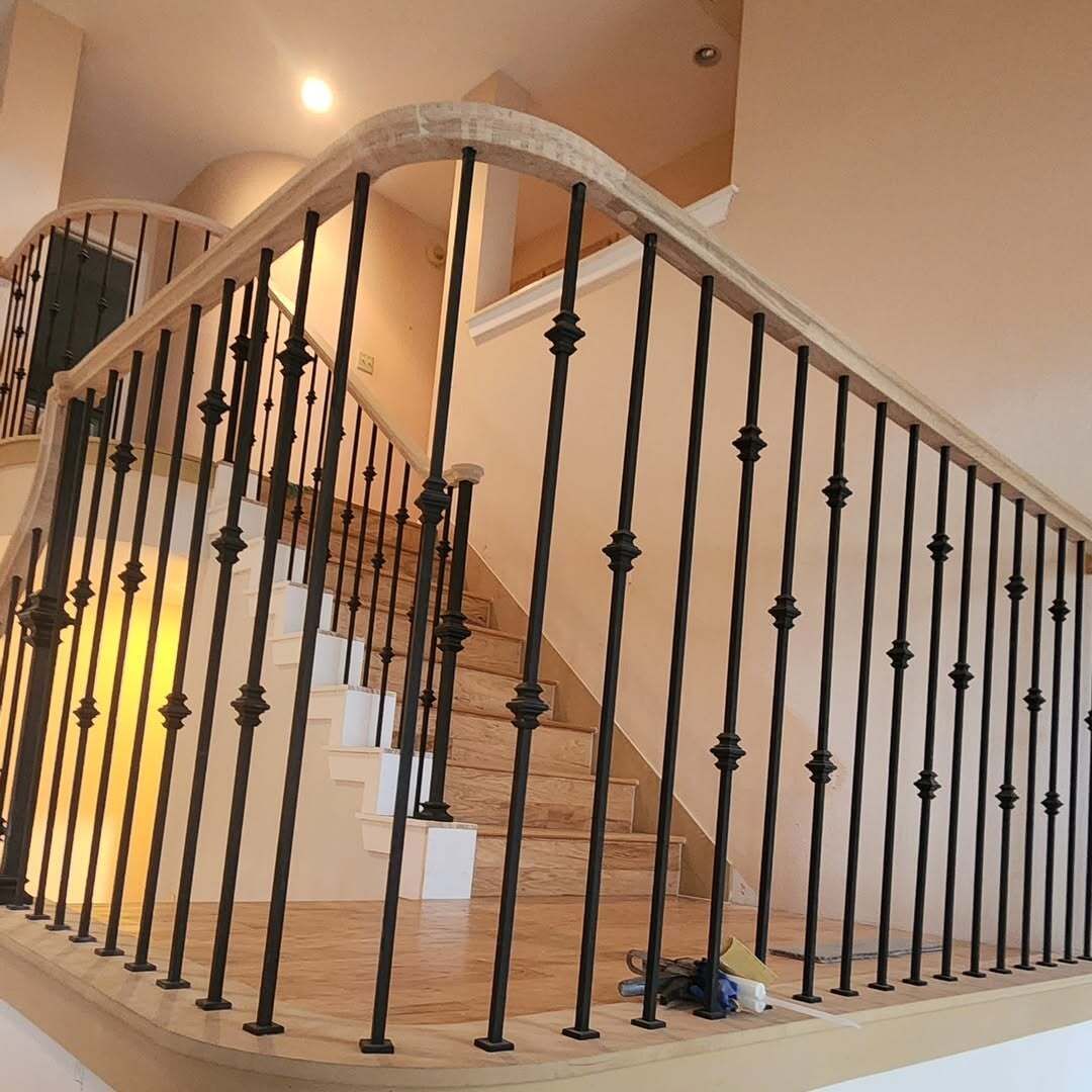 Indoor staircase with tan carpet, white banister, and black wrought-iron railings in a softly lit foyer