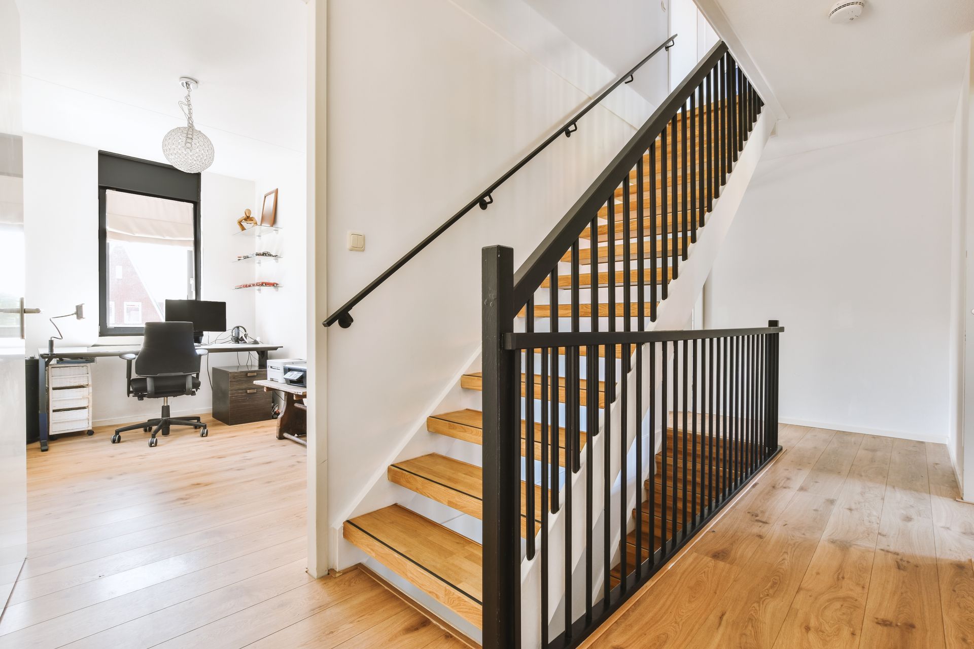 Modern home interior with staircase, black railing, and a home office in the background