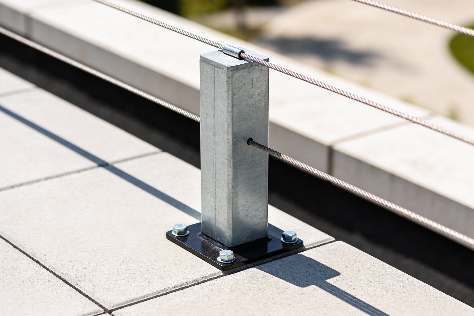 Metal railing post on a tiled rooftop terrace with a cable running across it.