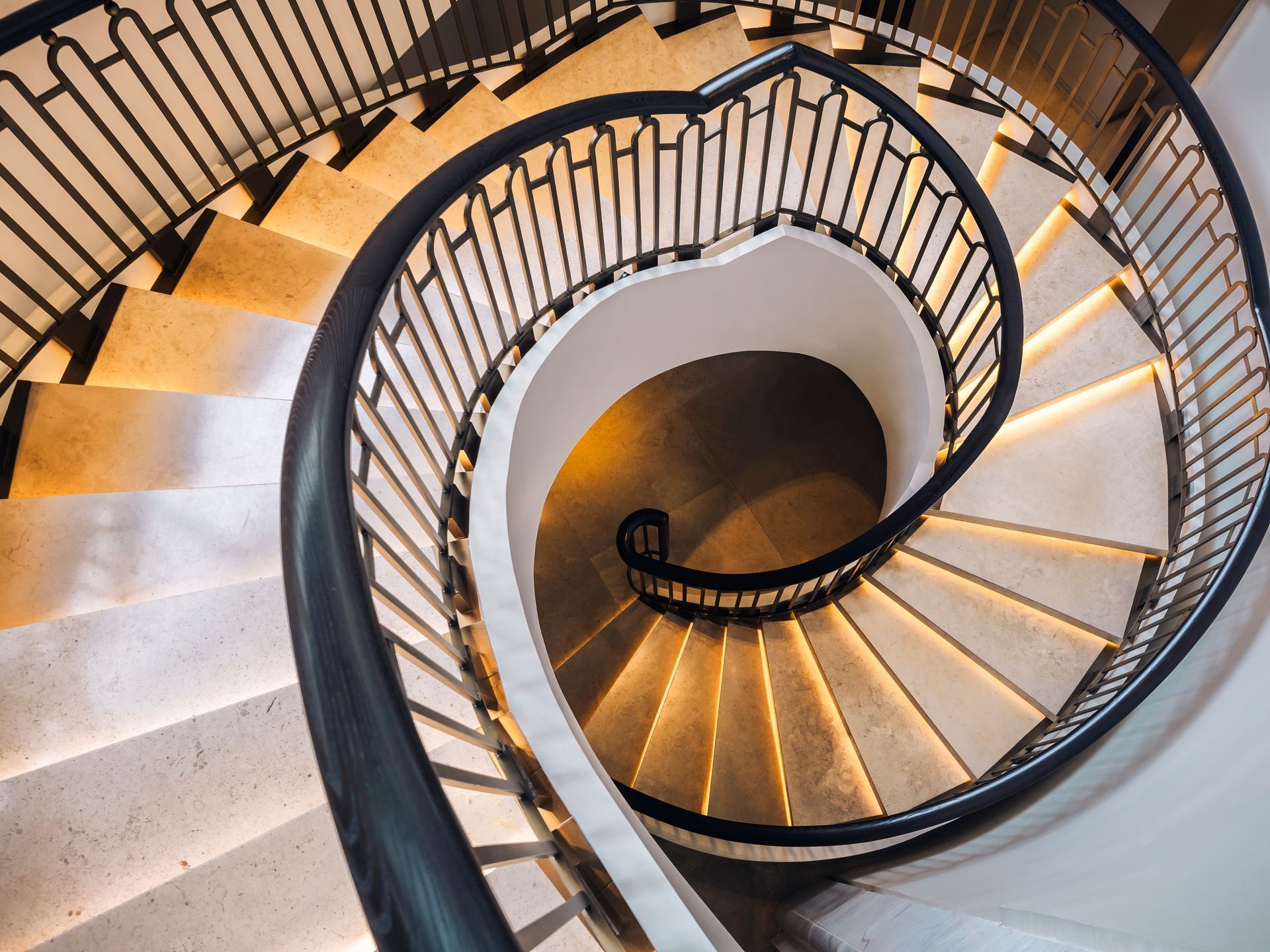 Spiral staircase with black railings and warm lighting, viewed from above.