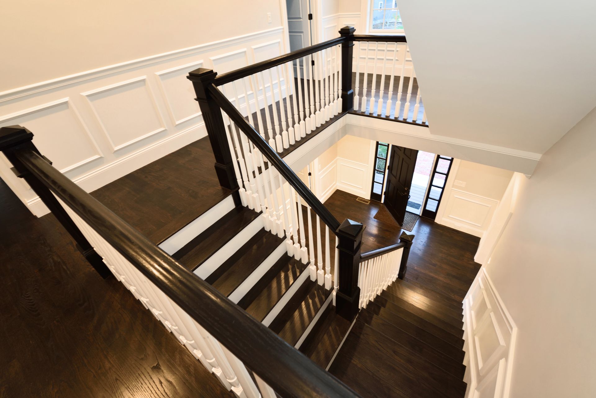 Staircase with dark wood railings and white walls in a bright hallway, viewed from above
