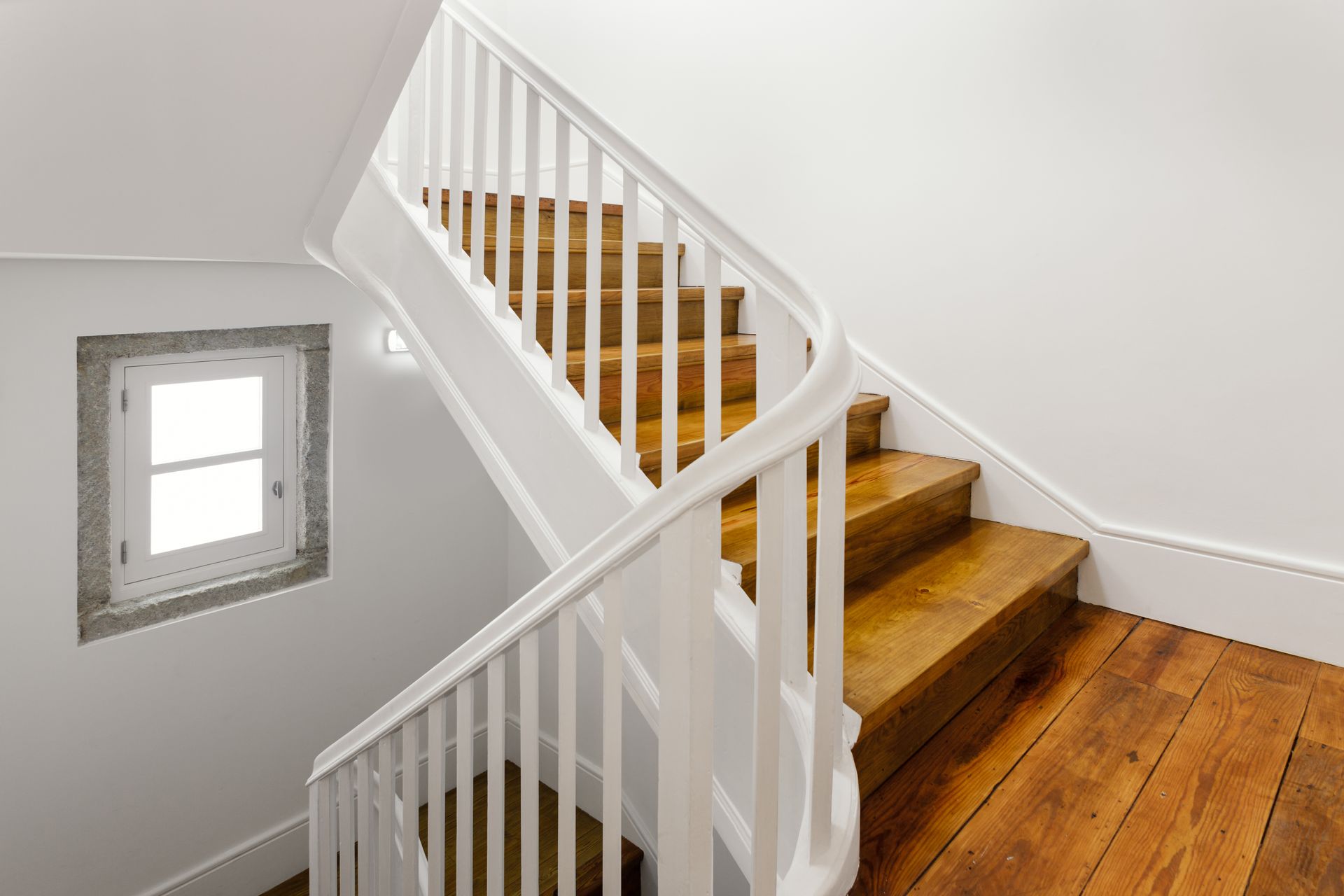 White staircase with wooden steps and railing beside a small window in a bright interior hallway