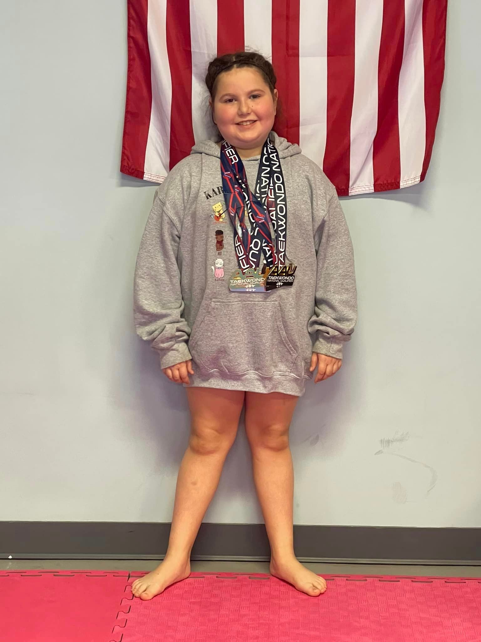 A young girl wearing a medal around her neck is standing in front of an american flag.