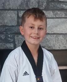 A young boy is wearing a karate uniform and a medal around his neck.