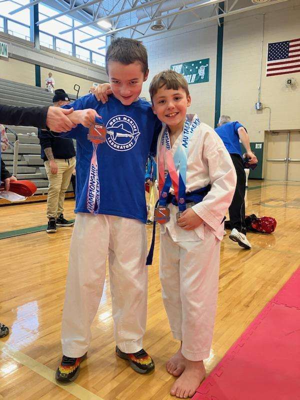 Two young boys are standing next to each other in a gym holding medals.