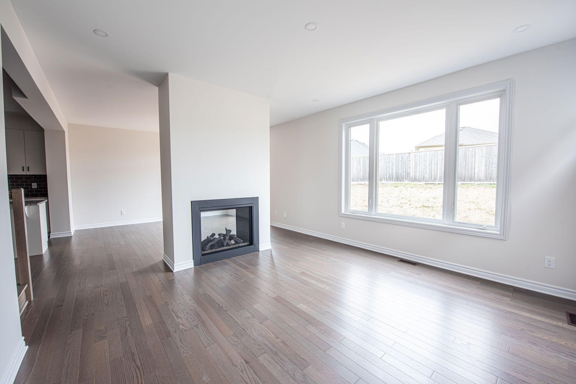 Empty living room with dark wood floor, fireplace, and window overlooking a yard.