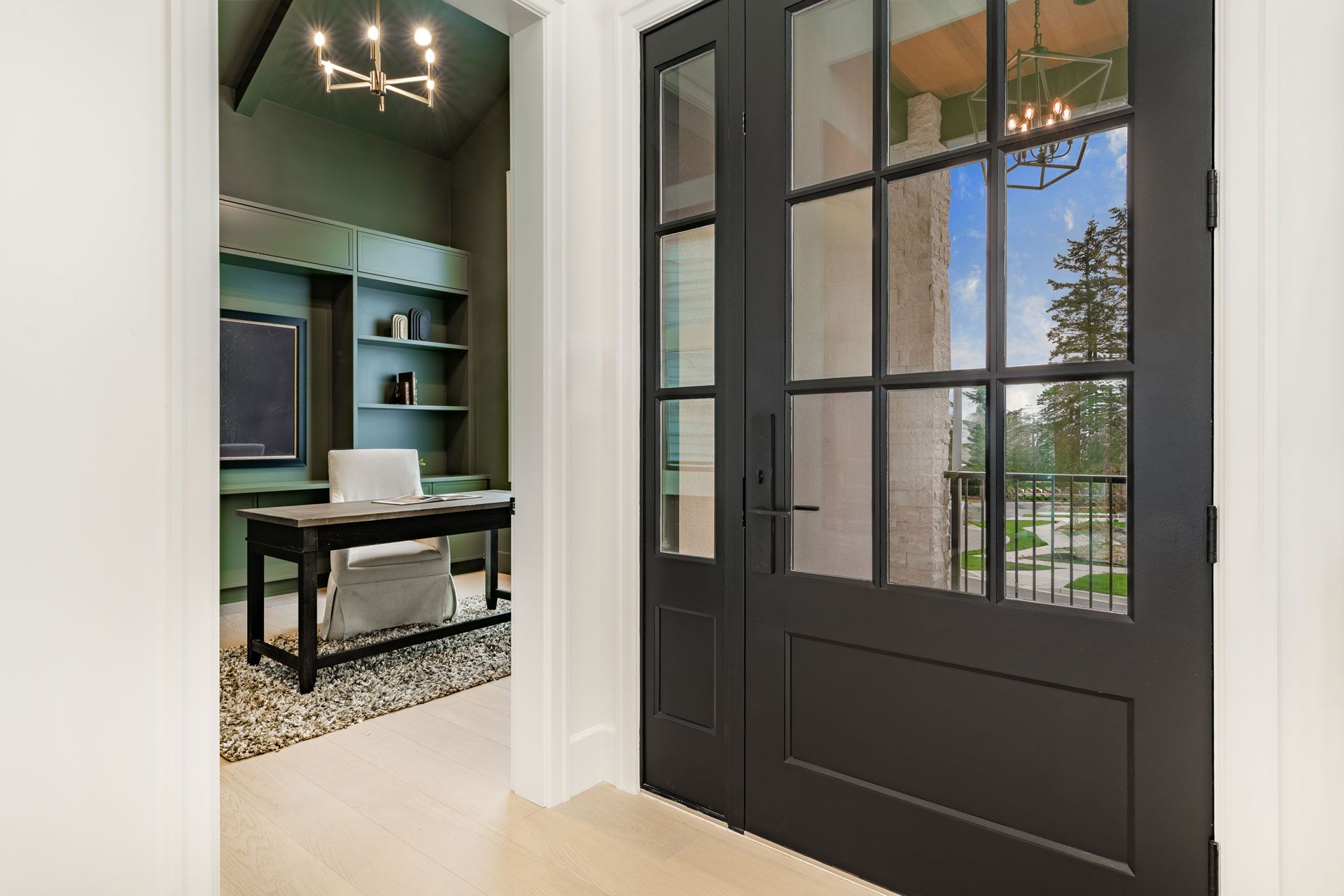 View of a home office through a black glass-paned door. The office has green walls and a desk.