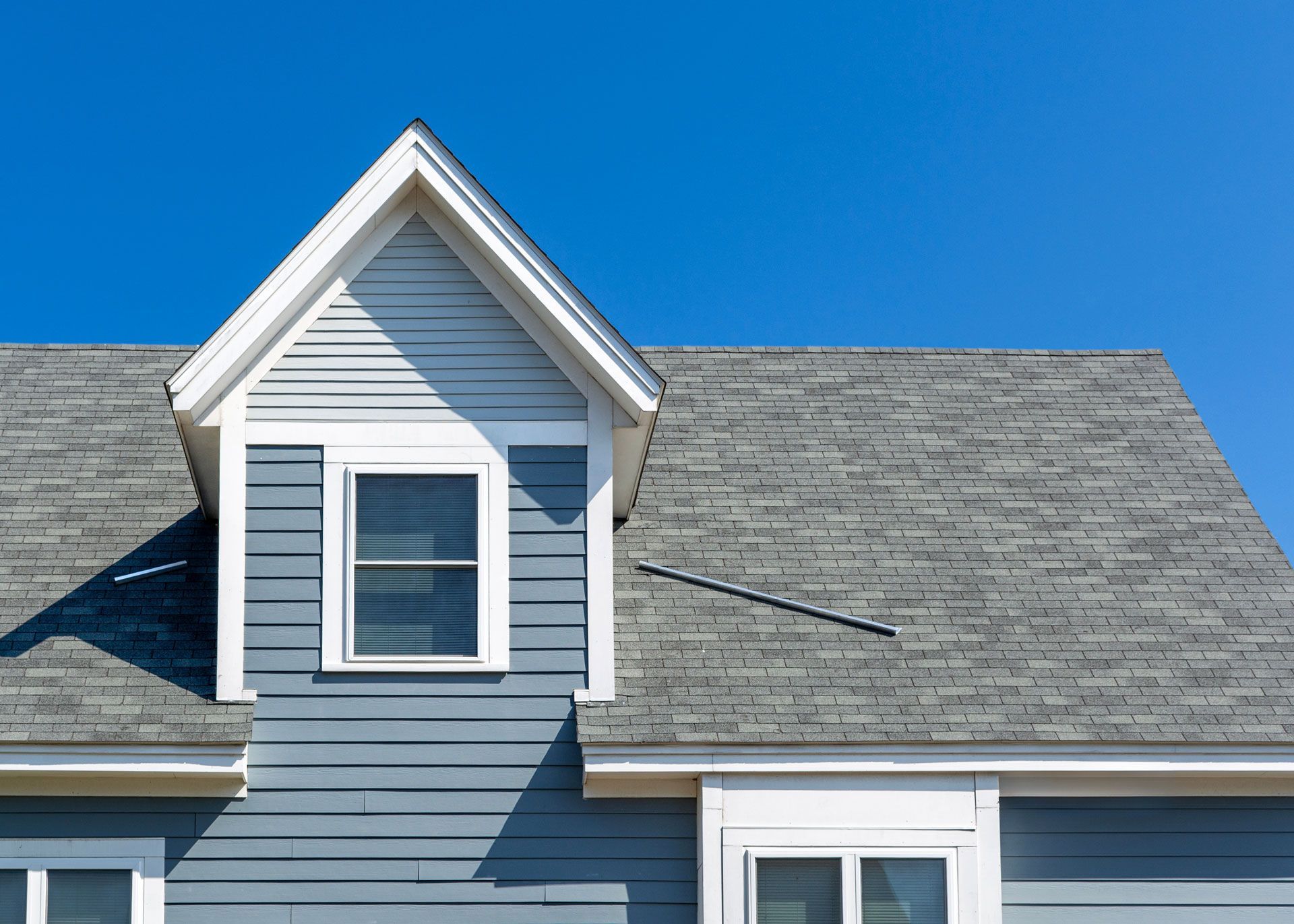Blue house with gray roof and dormer window against a bright blue sky.
