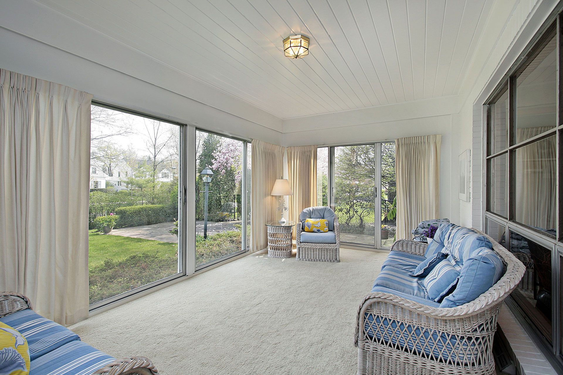 Sunroom with large windows, white walls and ceiling, wicker furniture, and a view of a yard.