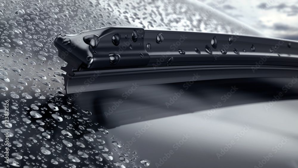 A close up of a wiper blade on a car windshield with water drops on it.