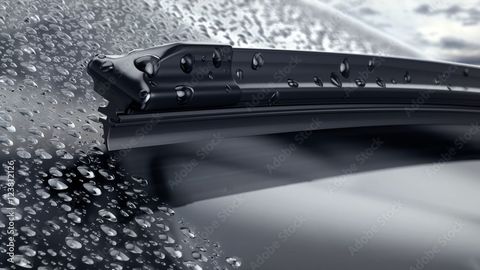 A close up of a wiper blade on a car windshield with water drops on it.