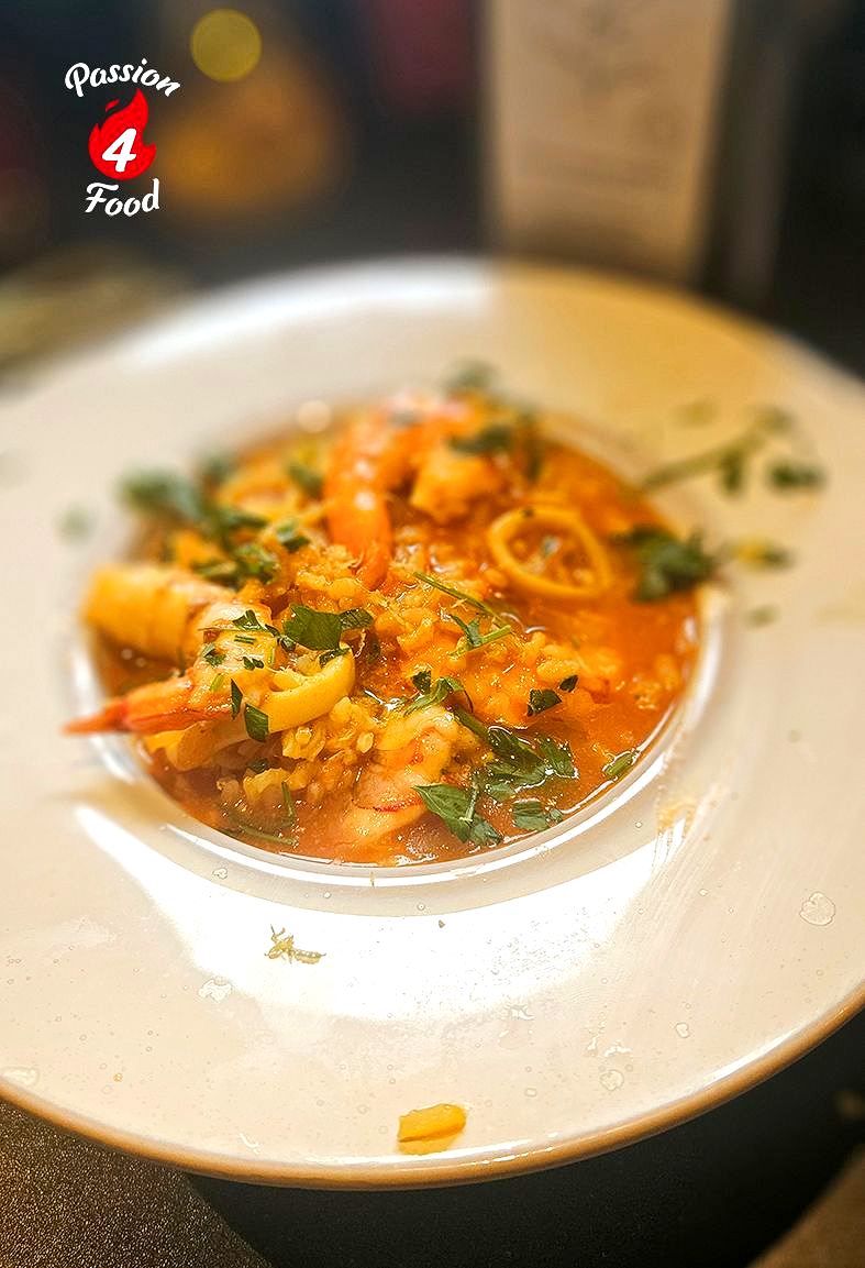 Een klein kommetje arroz meloso con calamari, gegarneerd met kruiden, op een wit bordje op tafel.