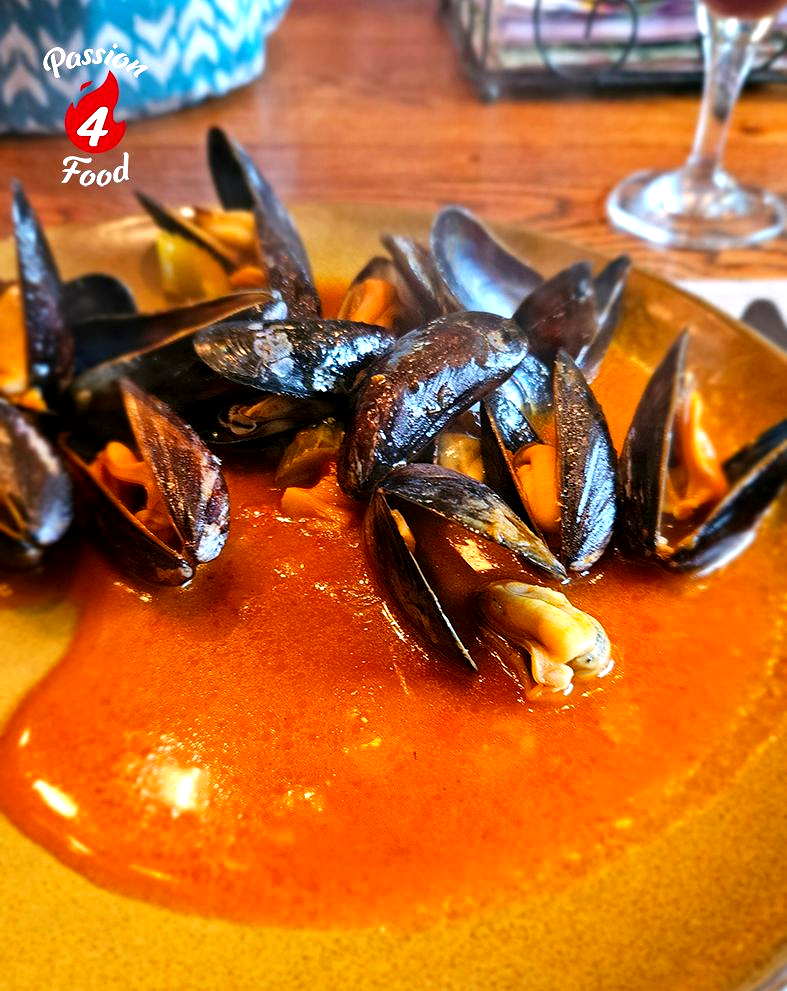 Mosselen in een felrode saus op een bord, met een houten tafel op de achtergrond.