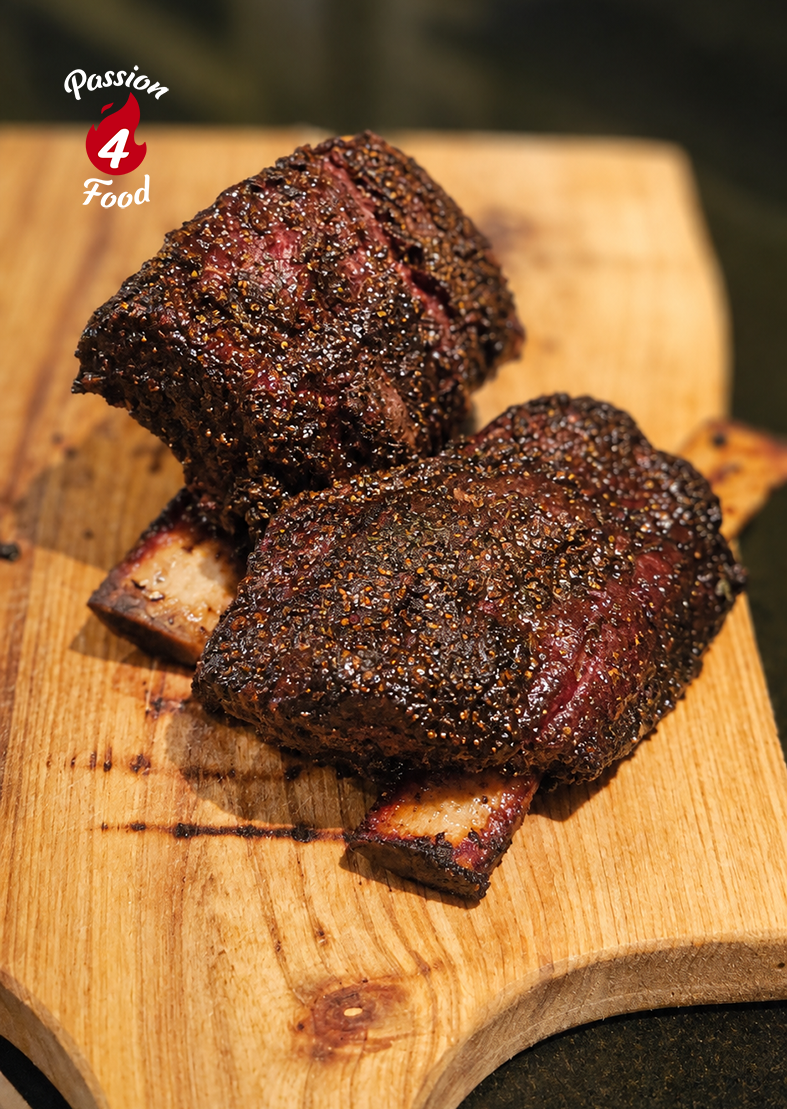 Two charred grilled meat chunks on a wooden cutting board with a small logo in the corner