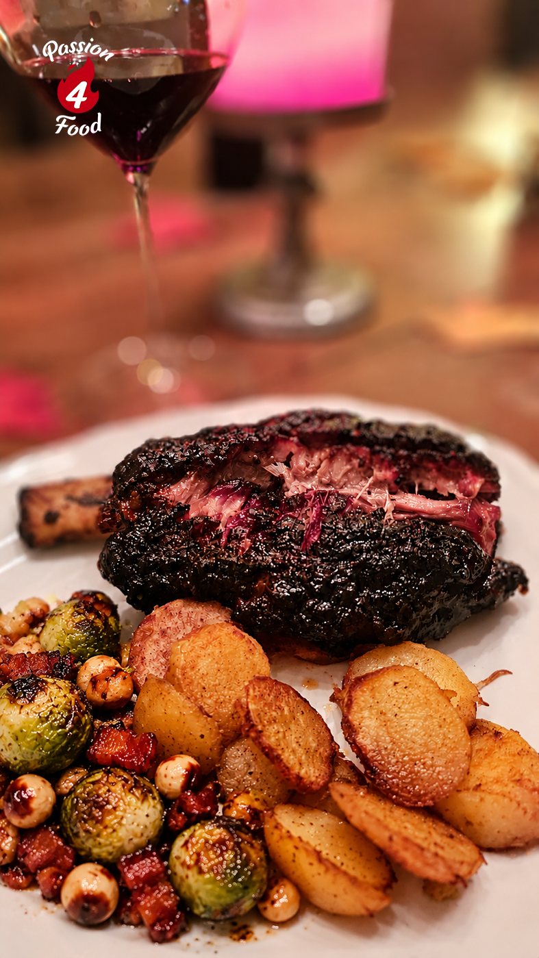 Gerookte shortrib op een bord met geroosterde groenten, met op de achtergrond een glas rode wijn