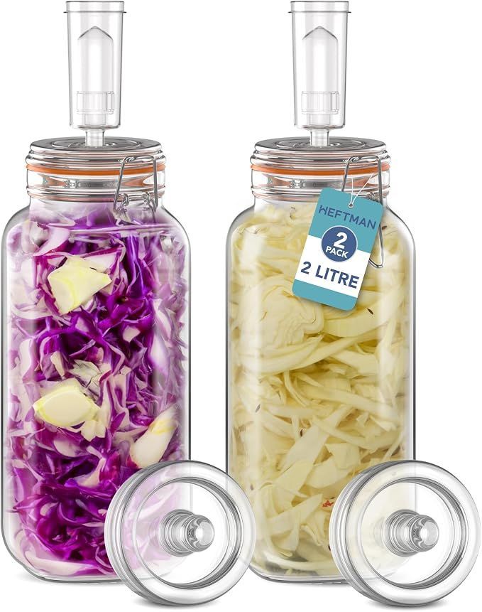 Two glass jars of pickled vegetables, one purple cabbage and one pale yellow onions, with lids beside them