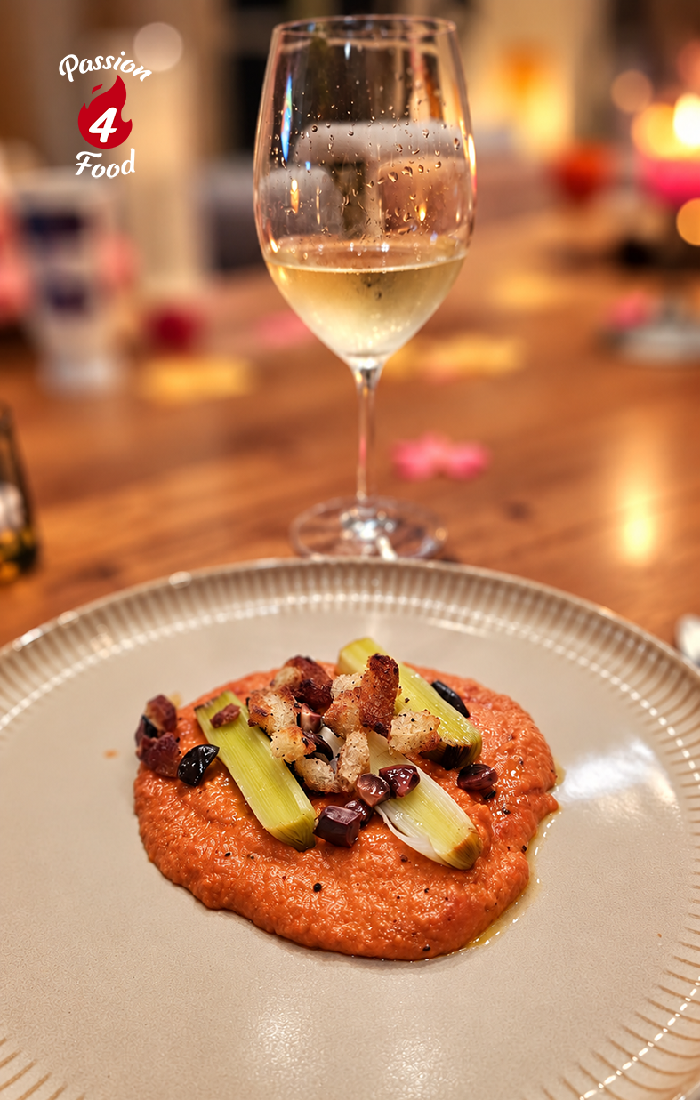Wijnglas achter een opgemaakt voorgerecht van rode puree, gegarneerd met groenten, op een restauranttafel