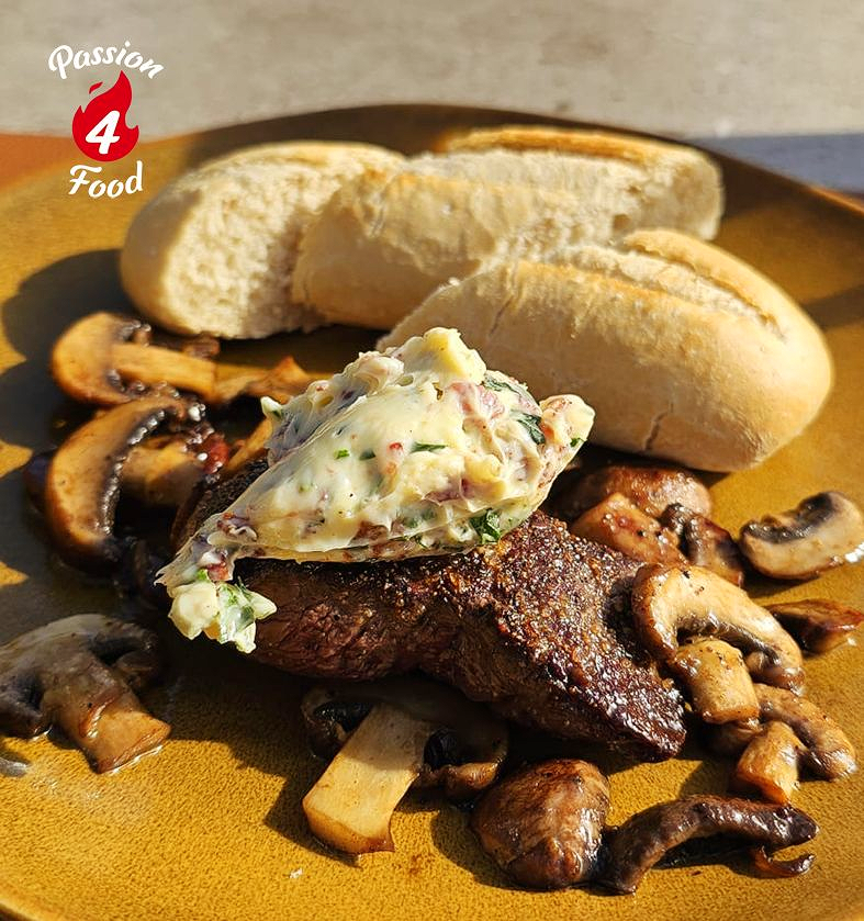 Gegrilde hertenbiefstuk met kruidenboter, champignons en brood op een bord.