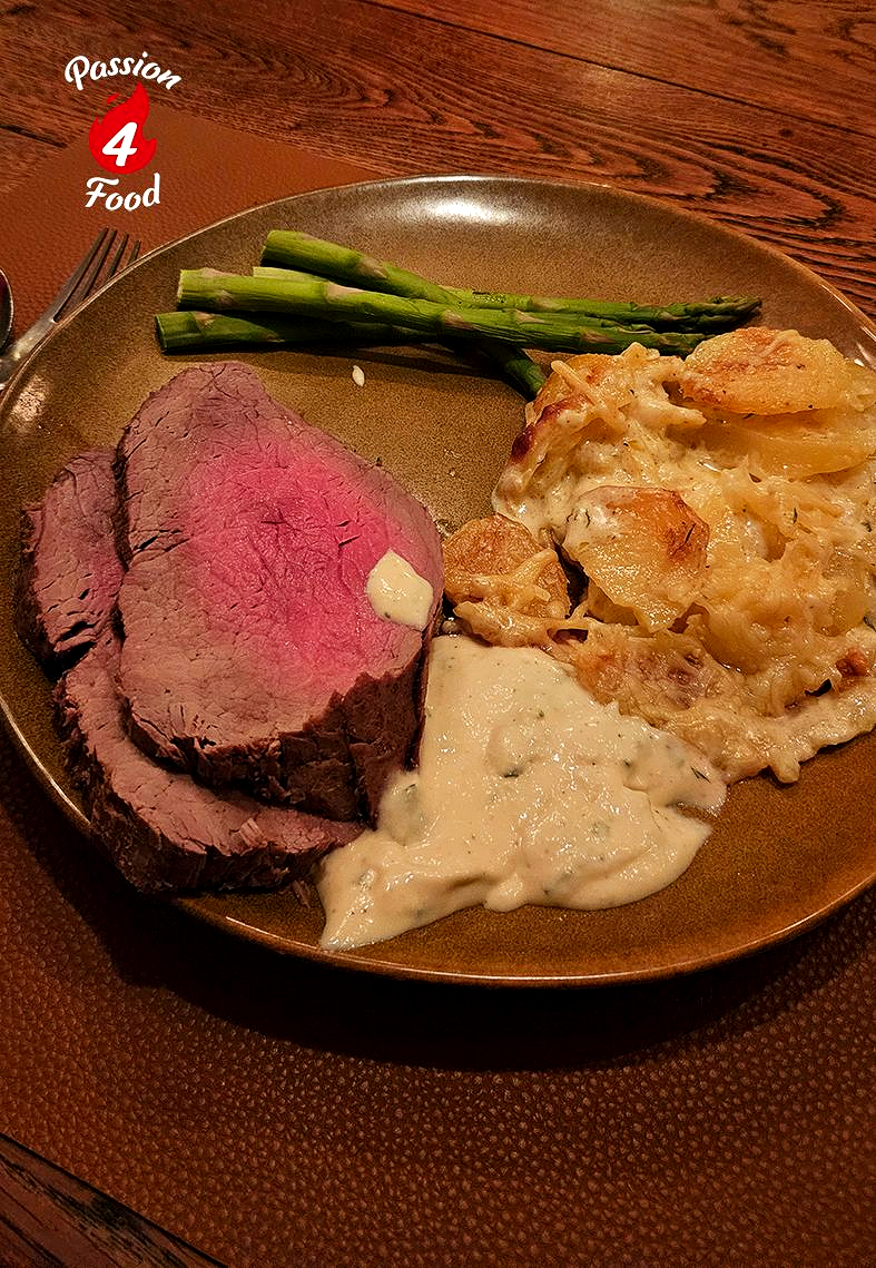 Geserveerd met ossenhaas, asperges, aardappelpuree en romige saus op een bruin bord.